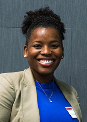 black woman in a blue shirt and tan blazer smiling