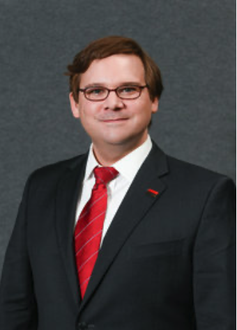 white man in a suit with a red tie and glasses smiling without teeth
