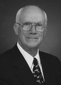 old, bald man in glasses and suit smiling without teeth showing