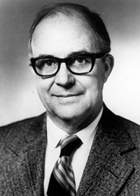 man in thick, dark rimmed glasses and a suit smiling