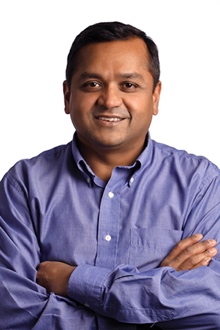 Mr. Arun Yethiraj. Indian man in a blue button down shirt smiling with his arms crossed.