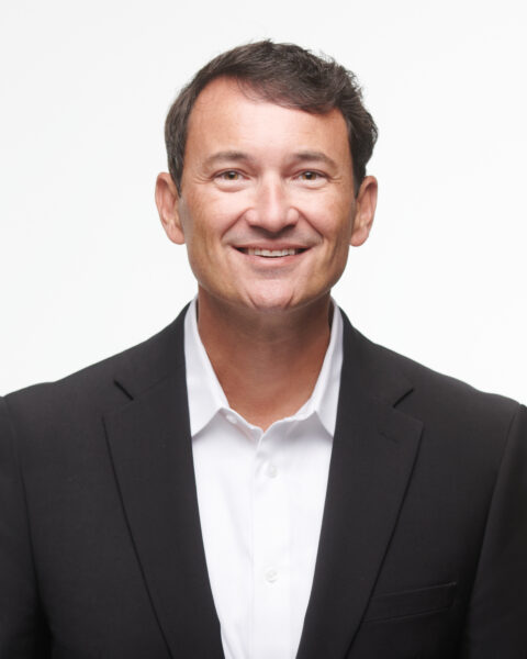 man in a white collared shirt and black blazer with dark hair smiling