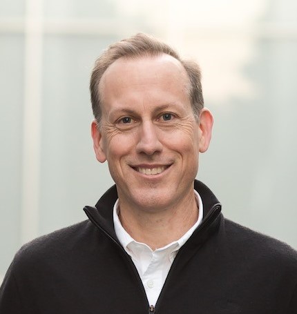 man smiling in a dark pullover and white collared shirt