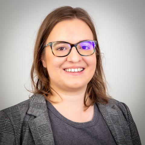 woman with brown hair wearing glasses and a grey suit smiling