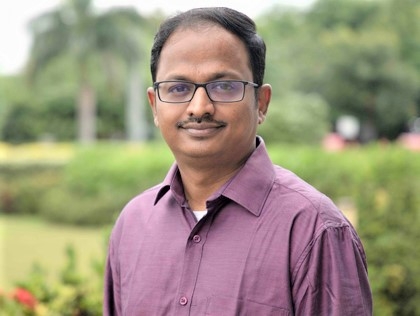 man wearing a red shirt and glasses standing outside and smiling at the camera