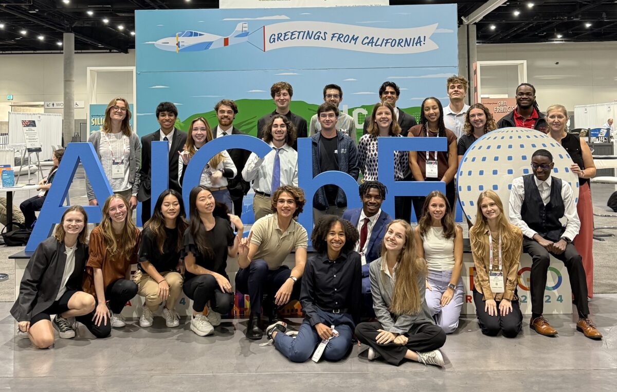 group photo of all CBE students in front of the AIChE logo inside of the conference