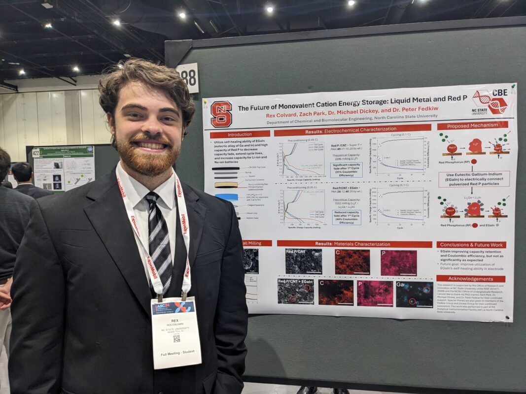 man wearing a suit standing next to a research poster