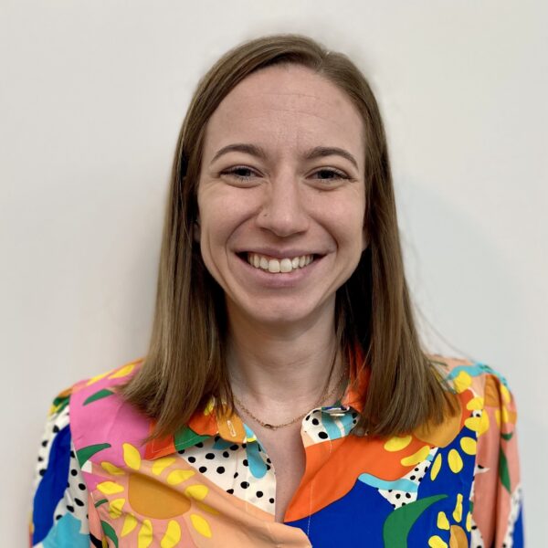 woman with medium length dark hair wearing a colorful blouse and smiling