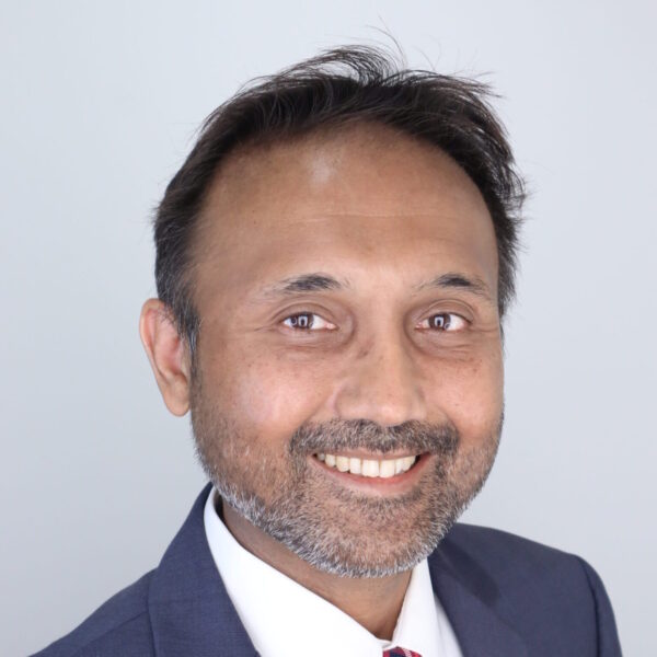 man with dark hair and stubble wearing a suit and smiling