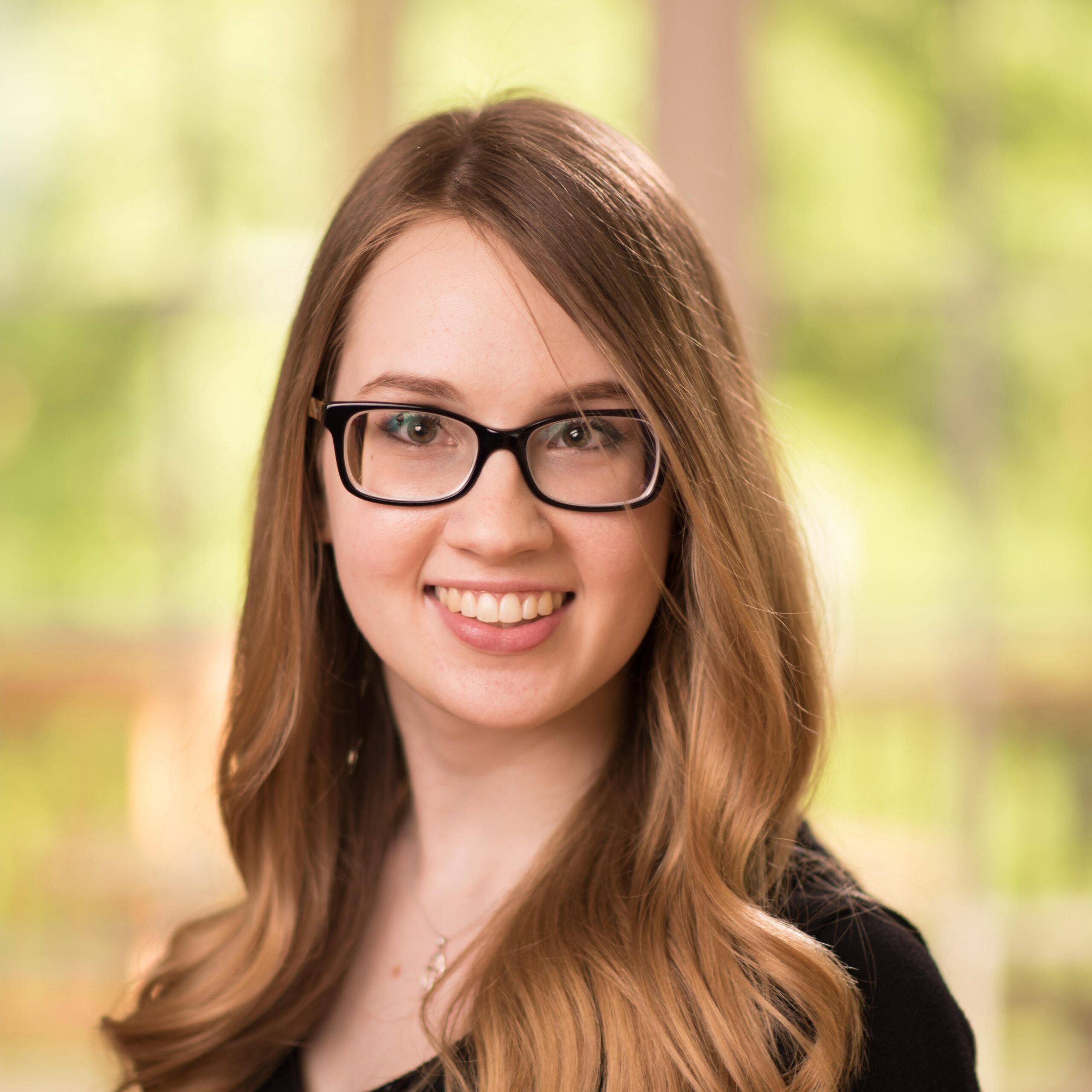 Woman with long hair wearing glasses and a black blazer and smiling