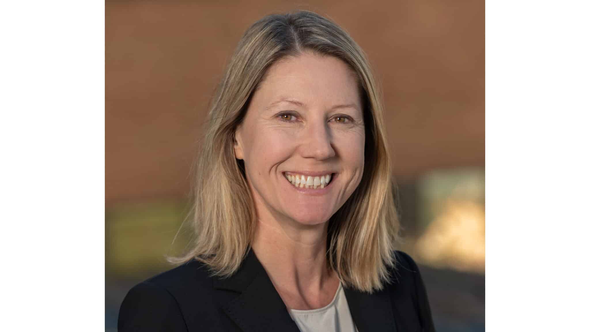 woman with short blonde hair wearing a black blazer smiling outside