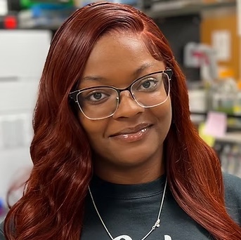 woman with red hair wearing glasses standing inside of a lab