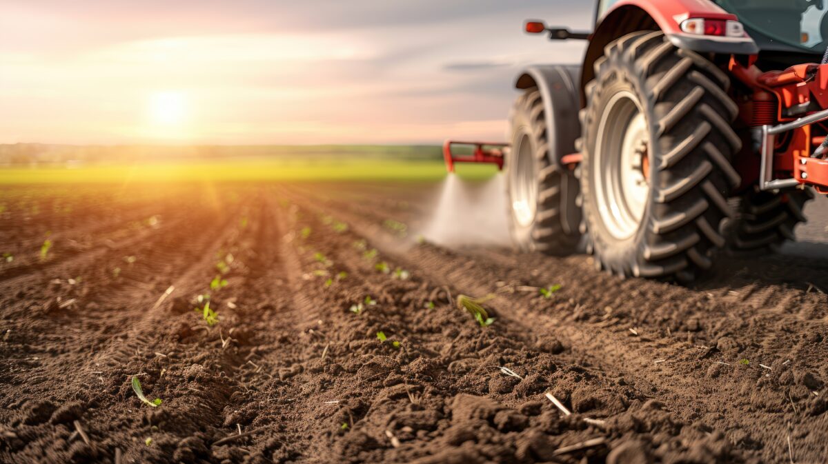 A tractor applies fertilizer to a field of soil. The white fertilizer is being sprayed in a line across the field. Generated with AI from Adobe Stock Images