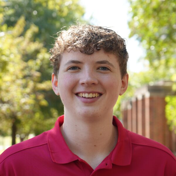 young man with short curly brown hair wearing a red polo and smiling