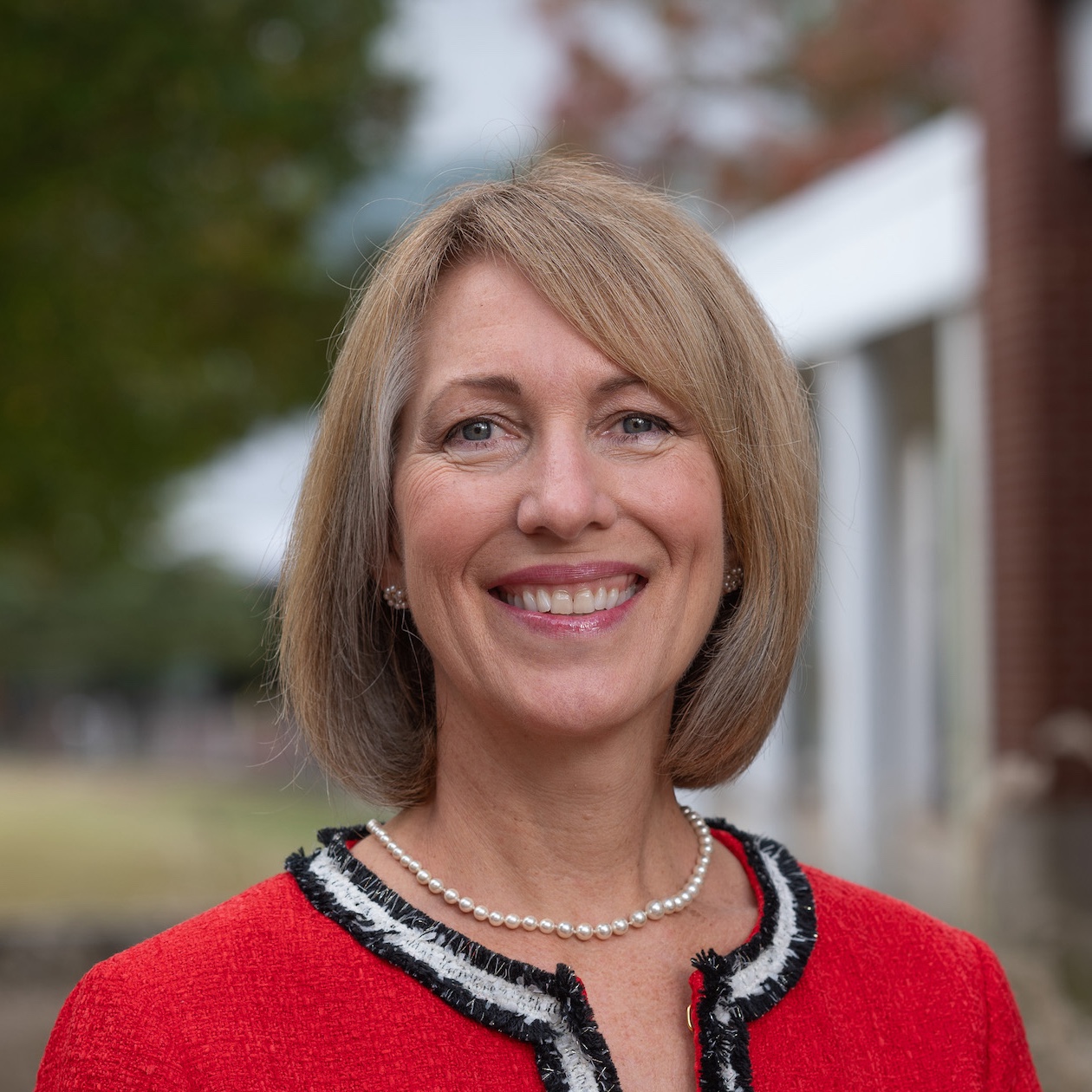 woman with short blonde hair wearing a red blazer and smiling