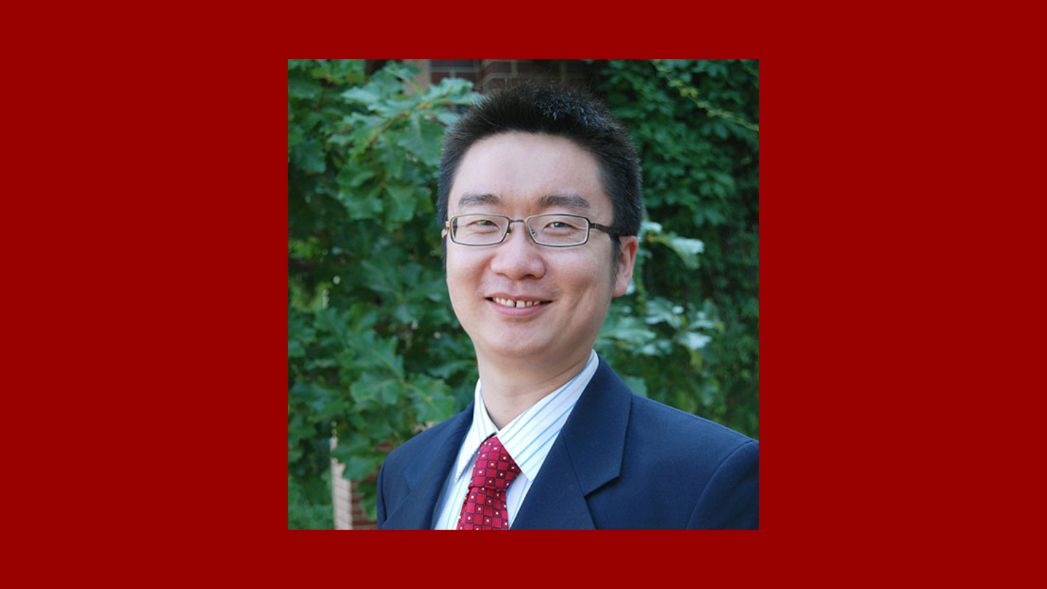 man with dark hair wearing glasses and suit smiling