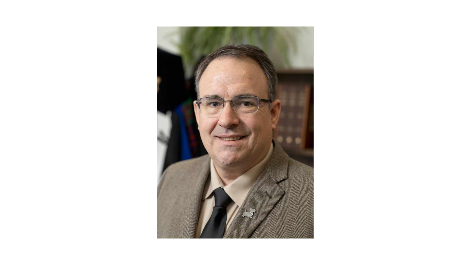 man with gray hair wearing a tan herringbone suit and glasses