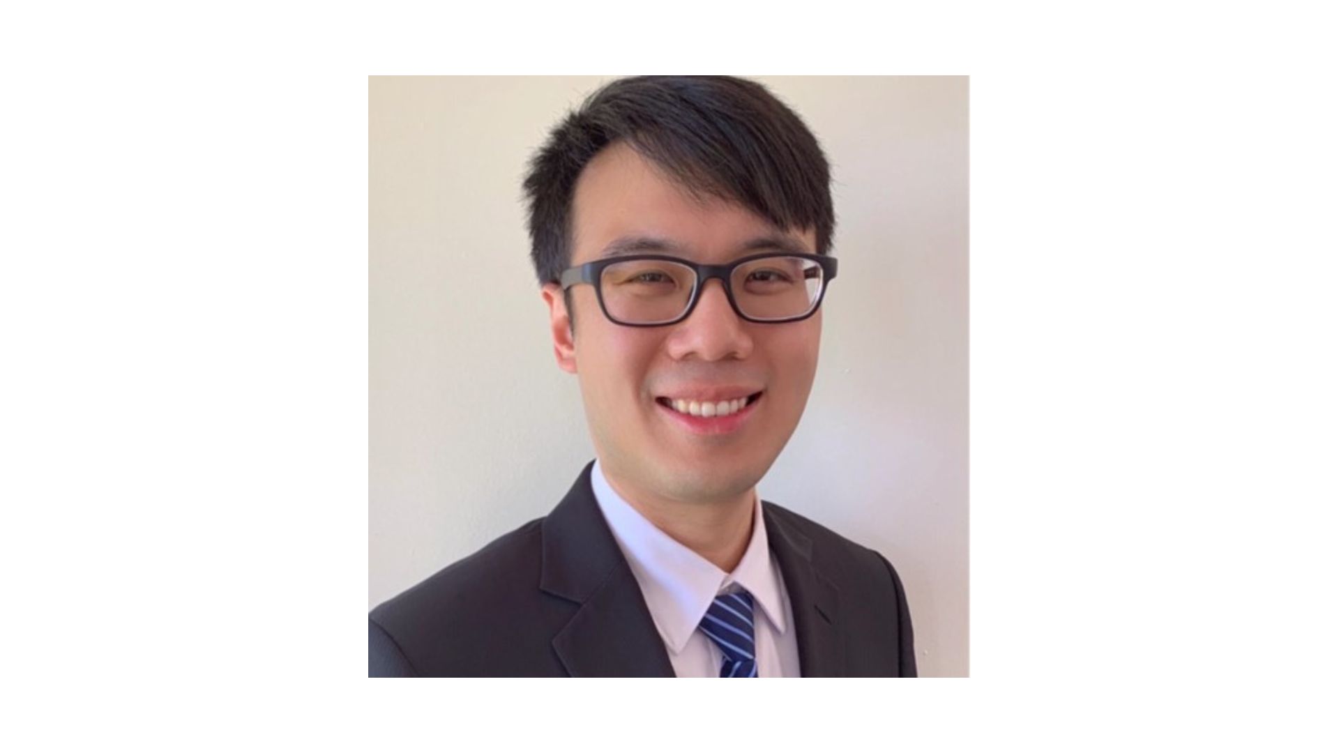 man with dark hair wearing glasses and a suit smiling