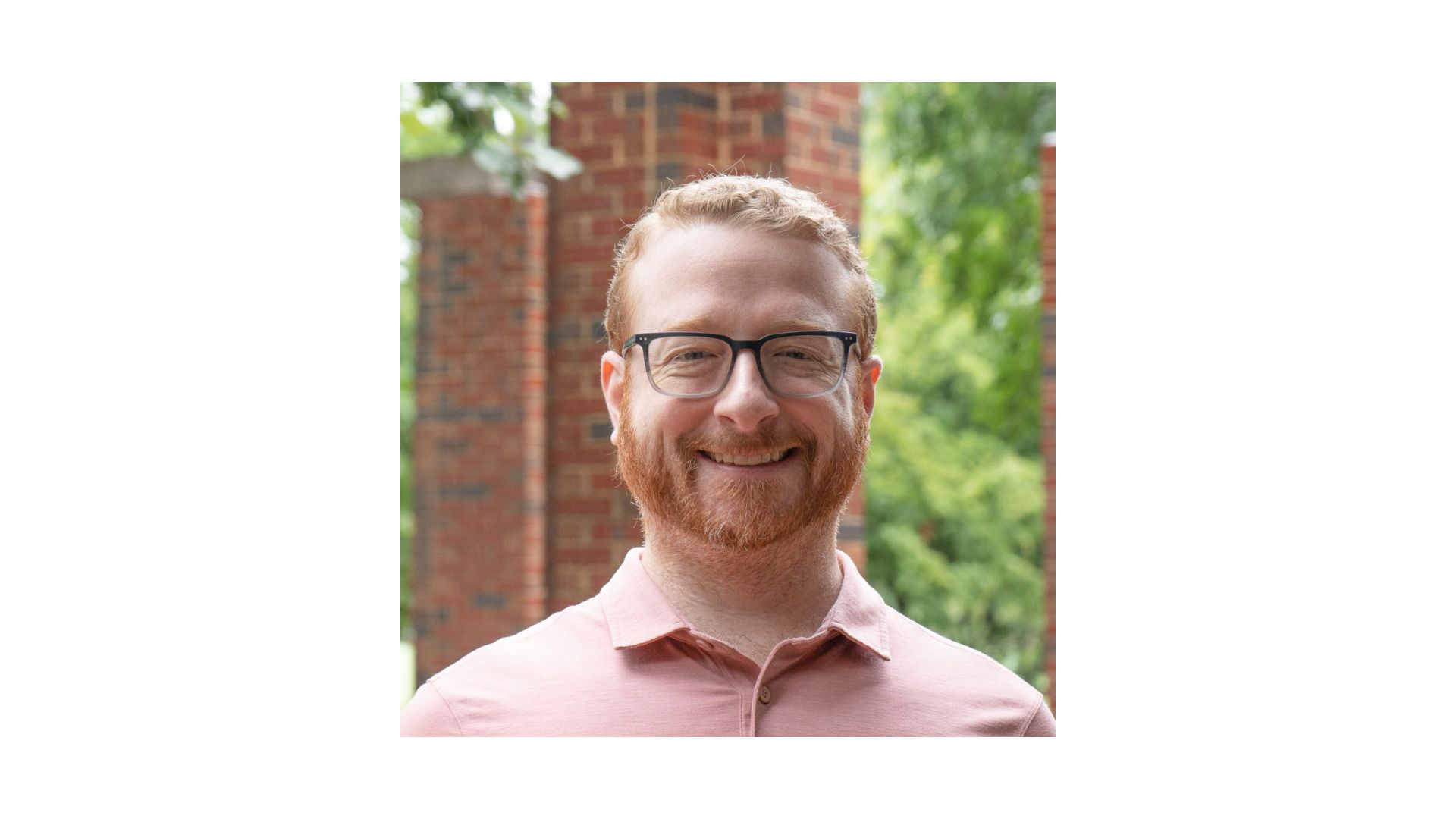 man with red hair and beard wearing glasses and a pink shirt