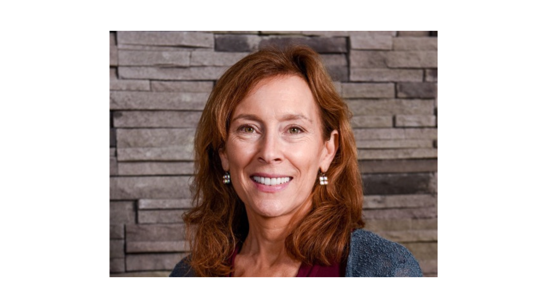 woman with red hair wearing a blue sweater and smiling
