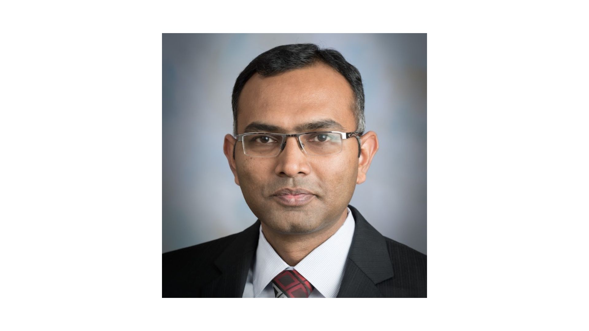 man with short dark hair wearing a suit and glasses