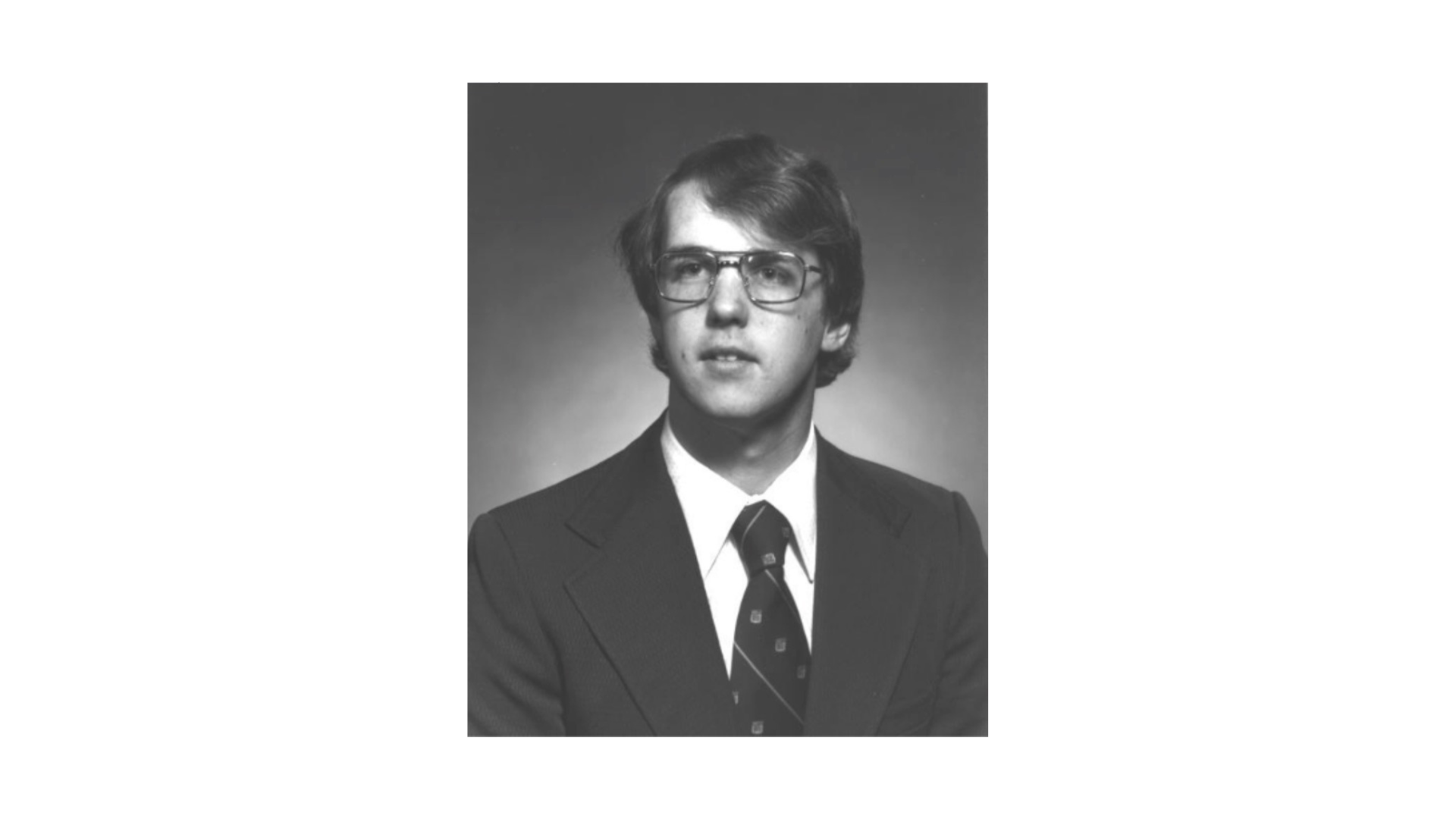 old black and white photo of a youn man with large glasses wearing a suit