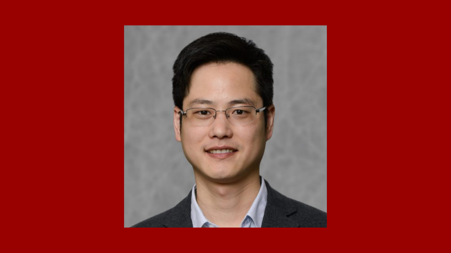 man with short dark hair wearing a suit and glasses and smiling