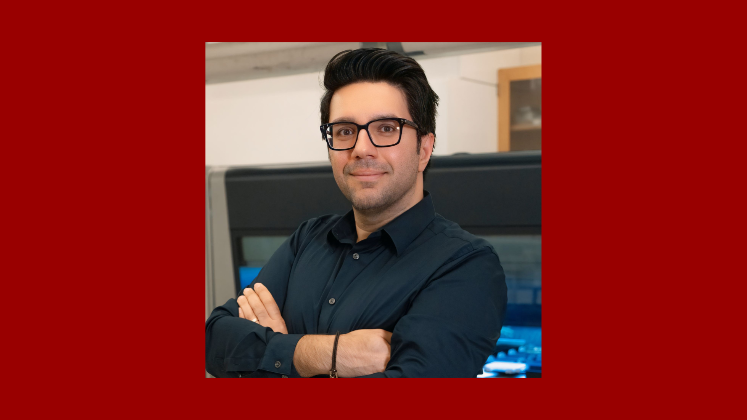 man with dark hair wearing glasses and standing with his arms crossed